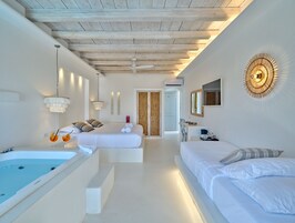 A modern bedroom with a large bed, a separate sitting area, a bathtub, and a wall-mounted light fixture.