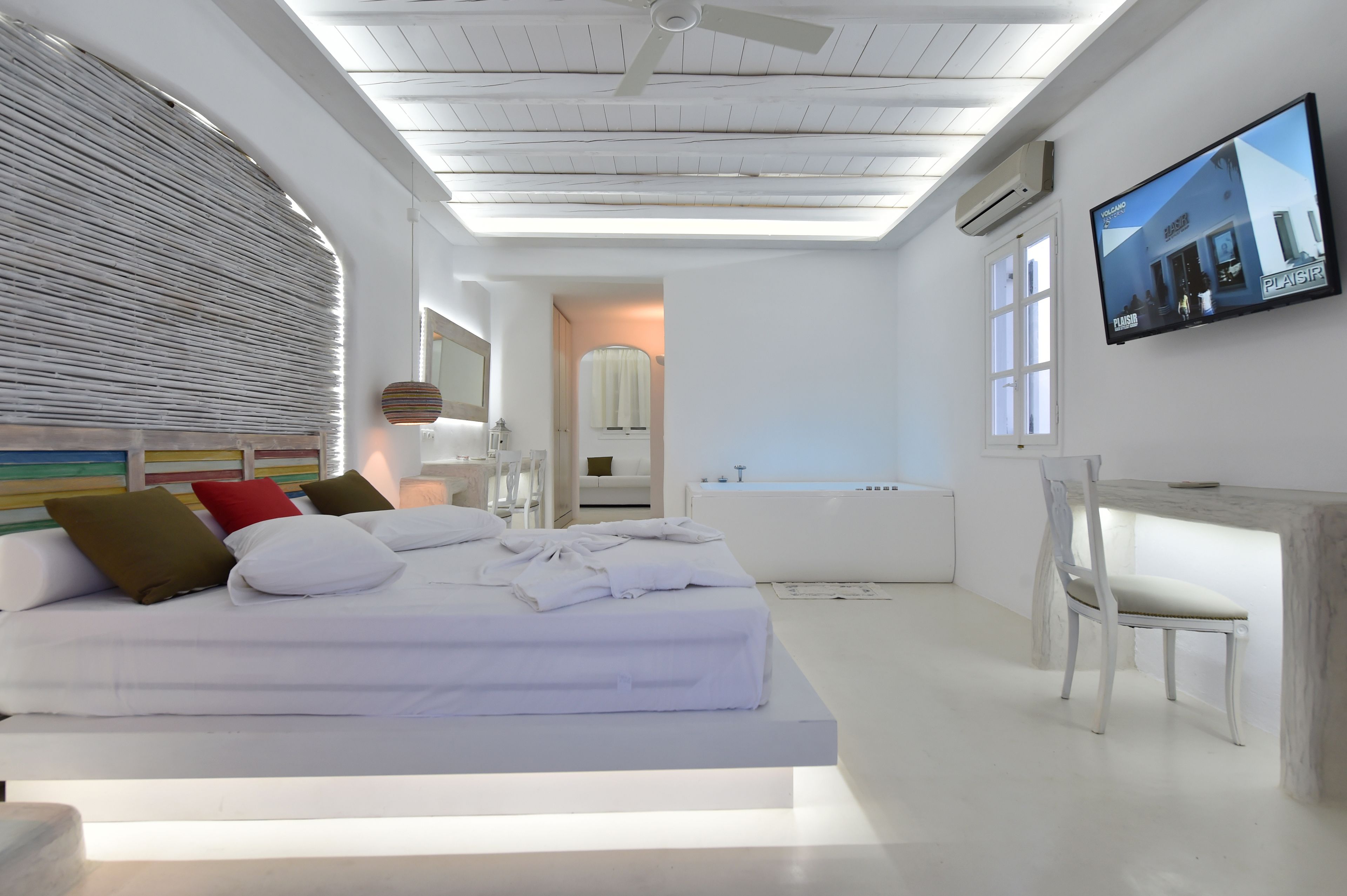 A modern hotel room with a large bed, a desk, and a television on the wall.