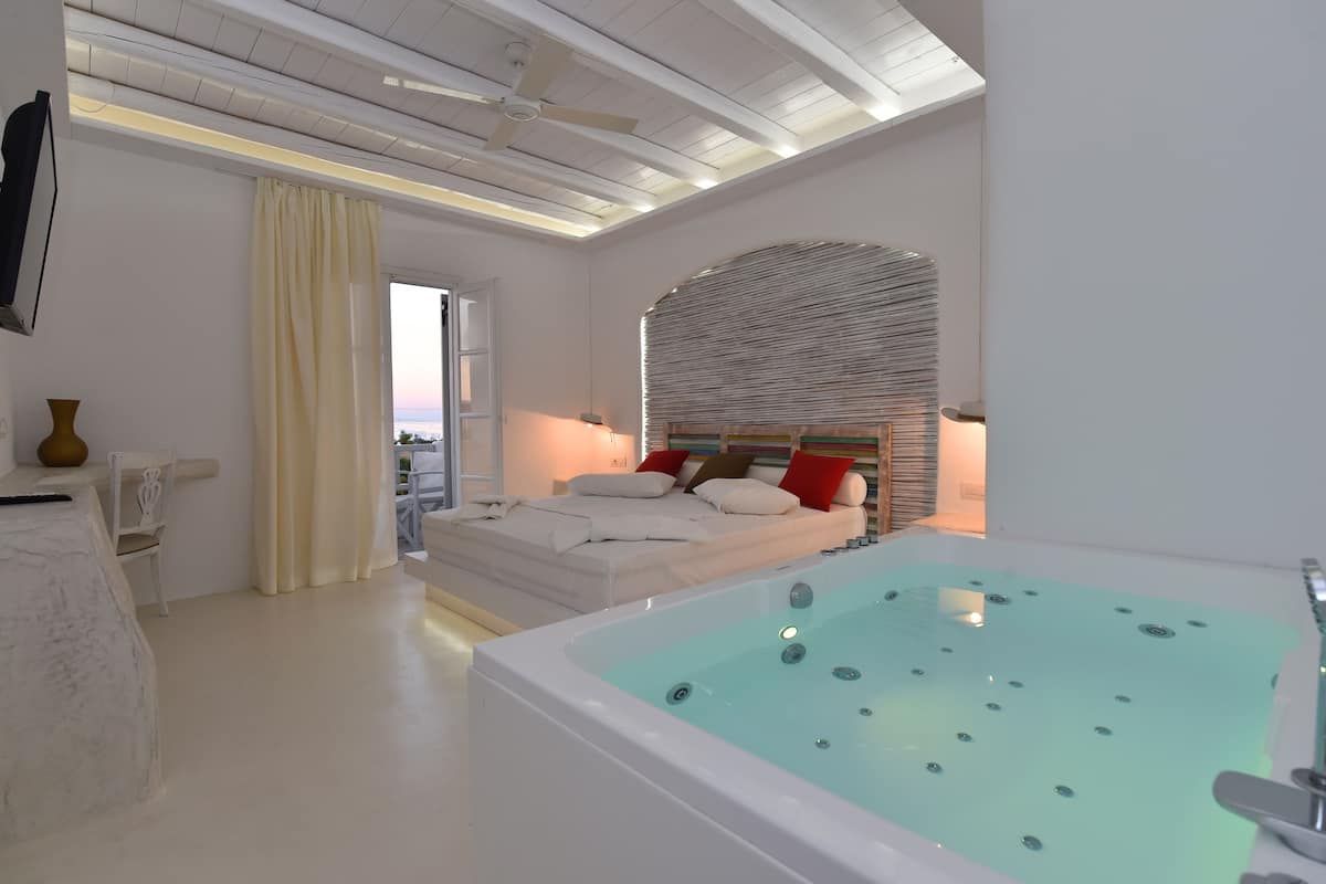 A modern bedroom with a large bed, a glass-enclosed jacuzzi, and a ceiling fan.