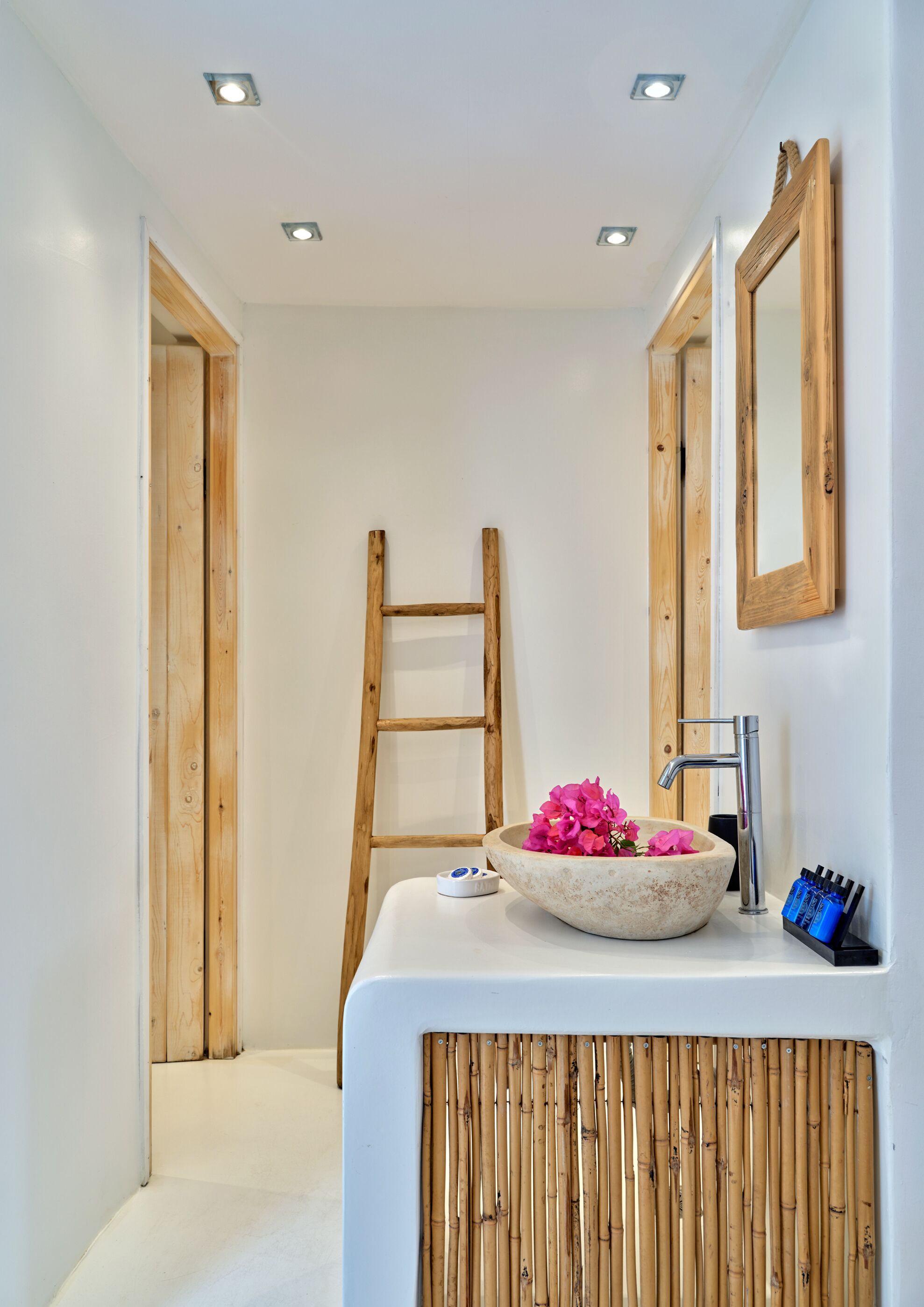 A bathroom with a wooden ladder, a white sink with a stone basin, and two wooden-framed mirrors.