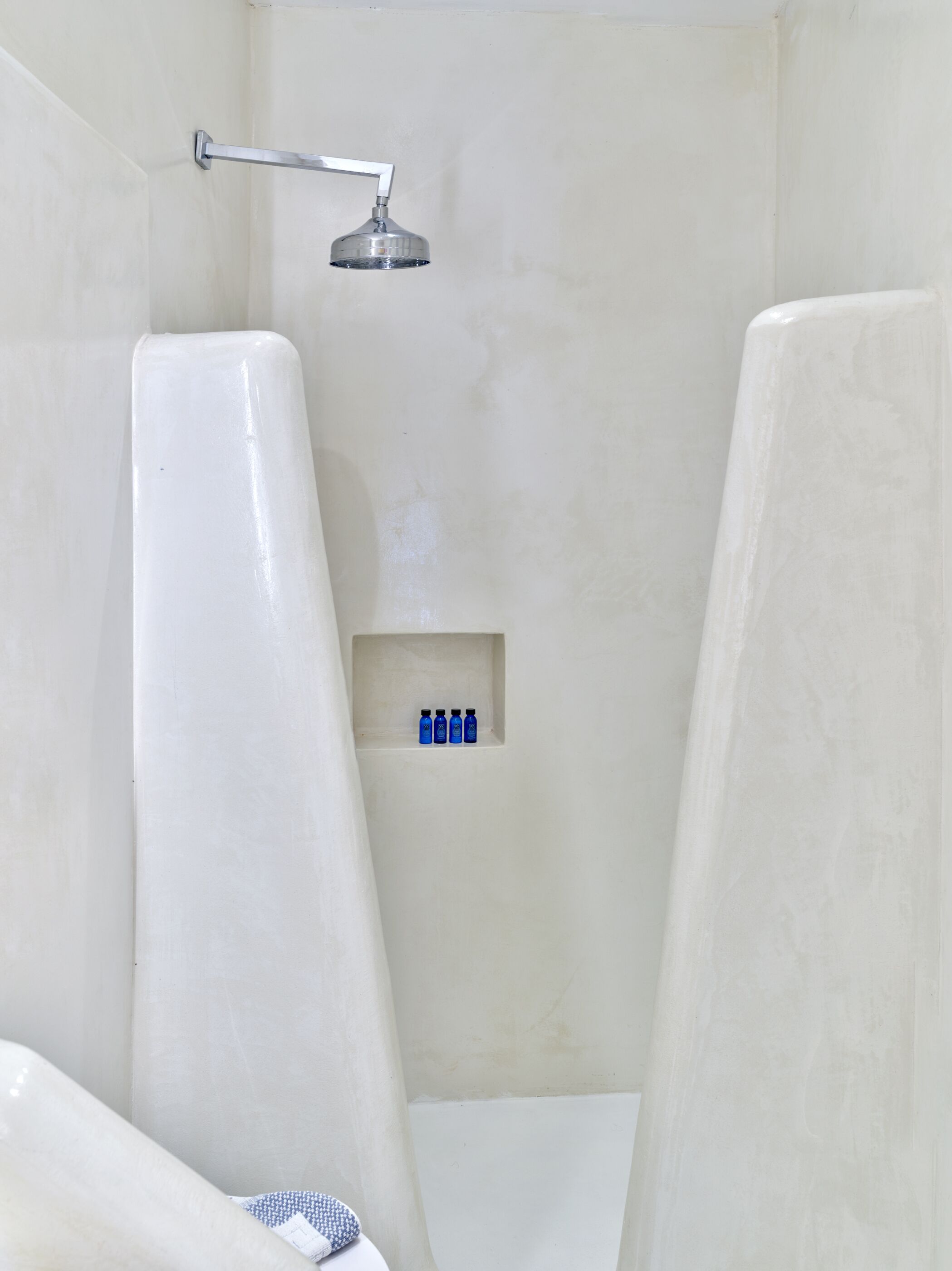 A bathroom with a shower, a white bathtub, and a shelf with blue bottles.