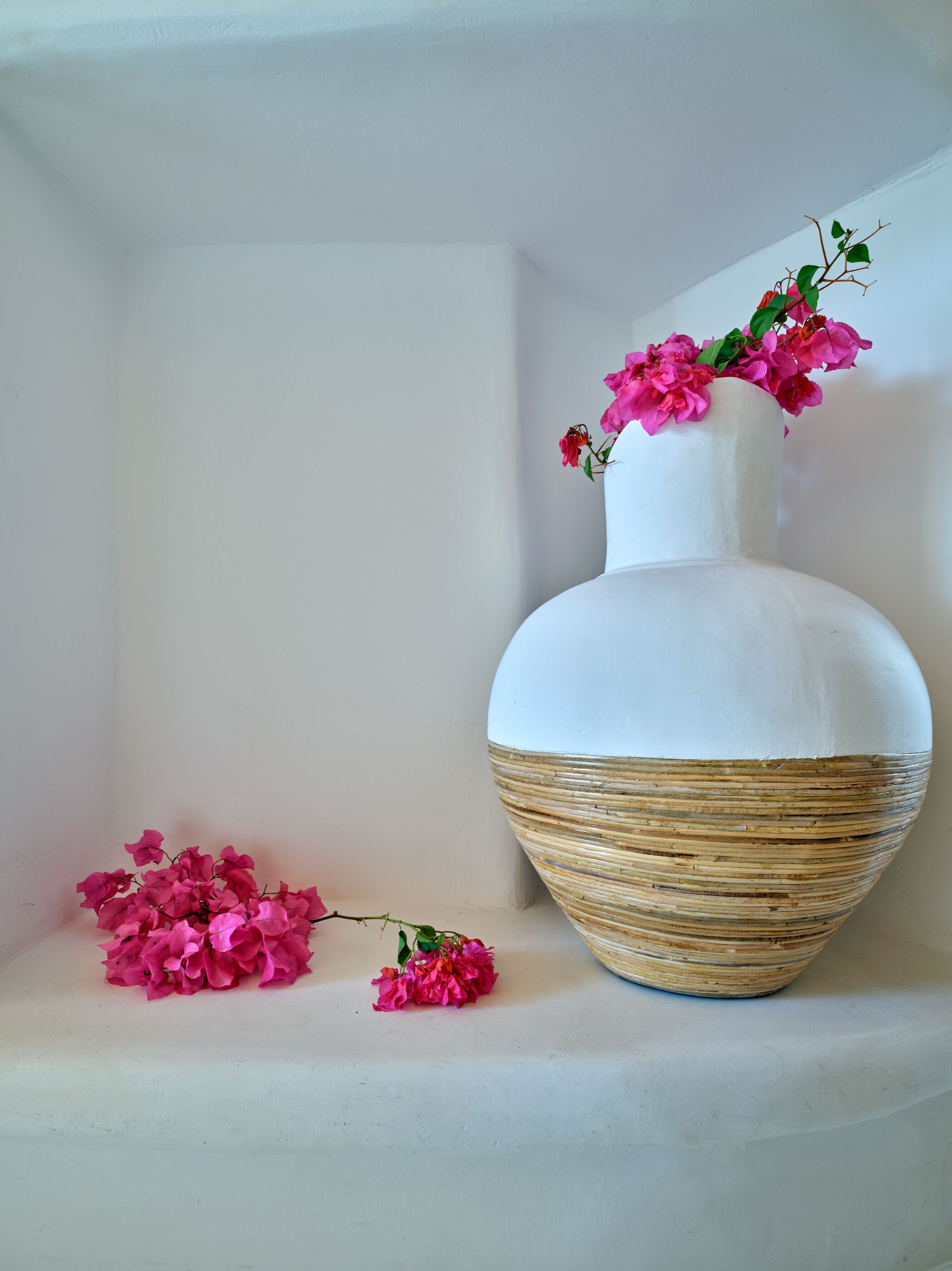 A white vase with pink flowers on a shelf.