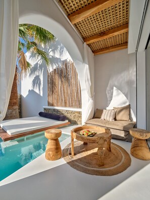 A sunlit room with a pool, wooden furniture, and a stone wall.