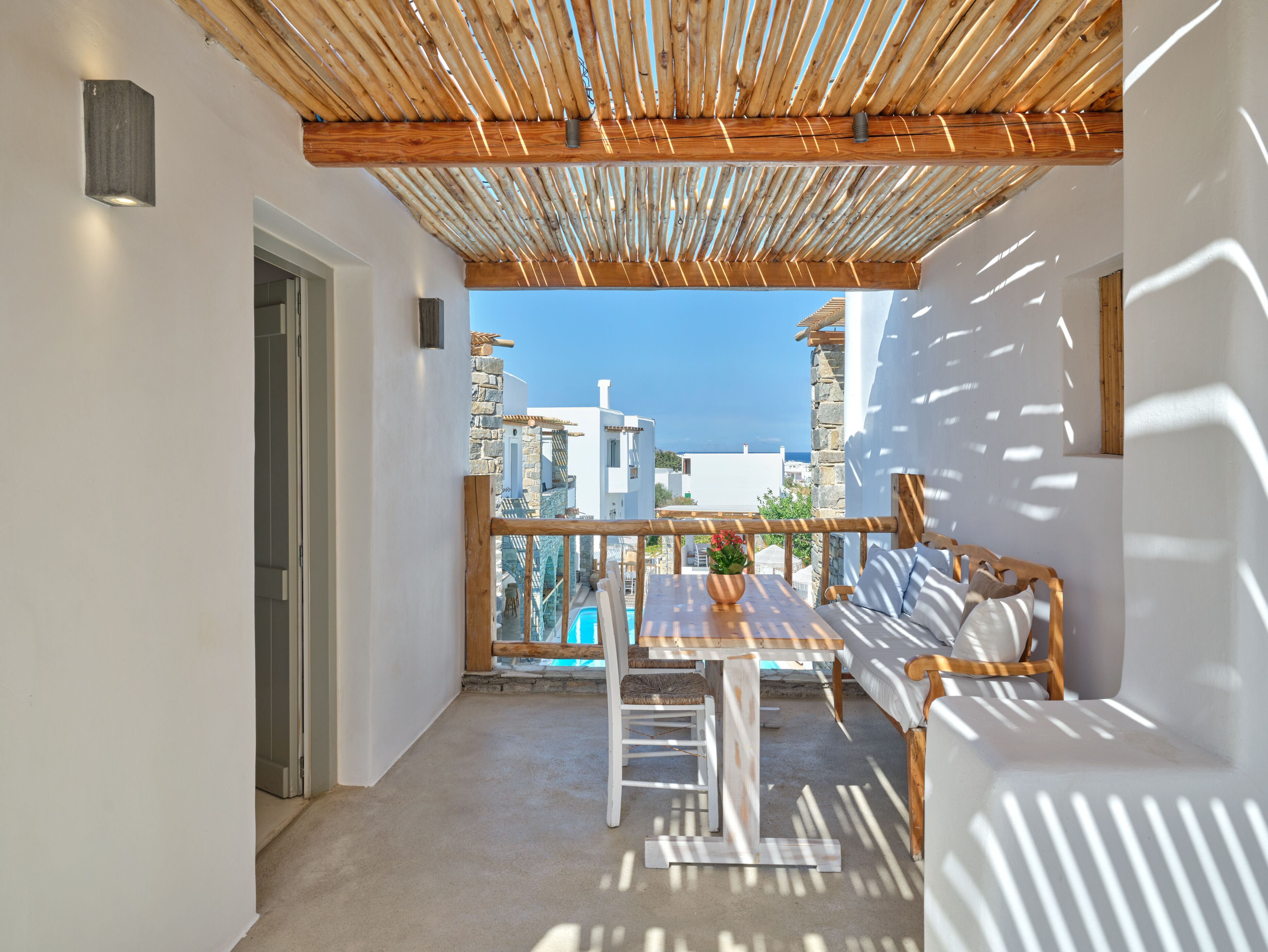 Un balcón con una pérgola de madera, mobiliario blanco y vistas al mar y edificios.