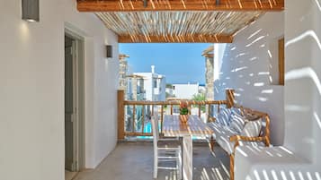 Un balcón con una pérgola de madera, mobiliario blanco y vistas al mar y edificios.
