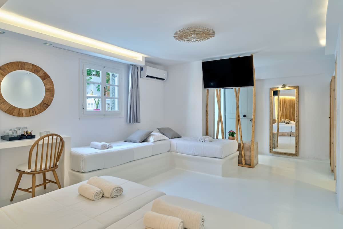 A modern hotel room with a large bed, a smaller bed, a desk with a chair, a TV, and a large mirror.