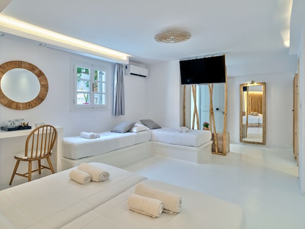 A modern hotel room with a large bed, a smaller bed, a desk with a chair, a TV, and a large mirror.
