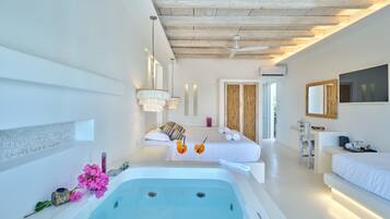 A modern spa room with a large bathtub, a sitting area with a sofa, and a desk with a chair.