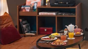 A cozy living room with a coffee table set for breakfast, featuring croissants, toast, kiwi, orange juice, and a teapot.