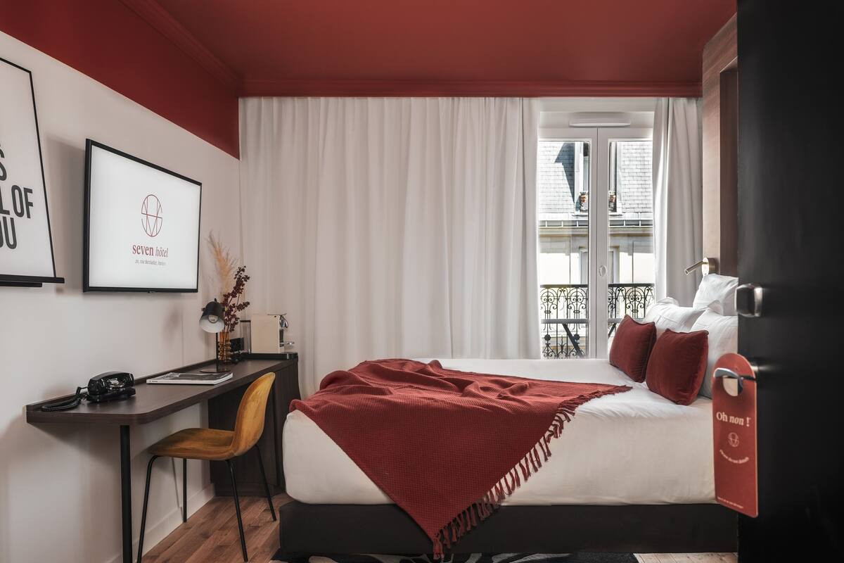 A hotel room with a bed, a desk, a chair, and a window with curtains.