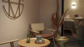 Une pièce chaleureuse avec une table ronde en bois, une chaise en osier, une œuvre d’art abstraite accrochée au mur et un lit avec une table de chevet.