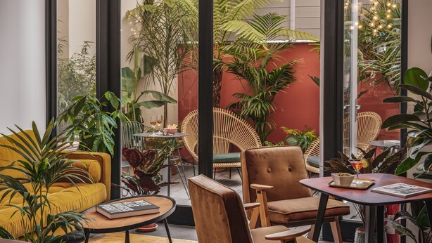 A cozy indoor seating area with a yellow sofa, a wooden chair, and a small table with a book and a drink. - Seven Hotel Paris (Paris)