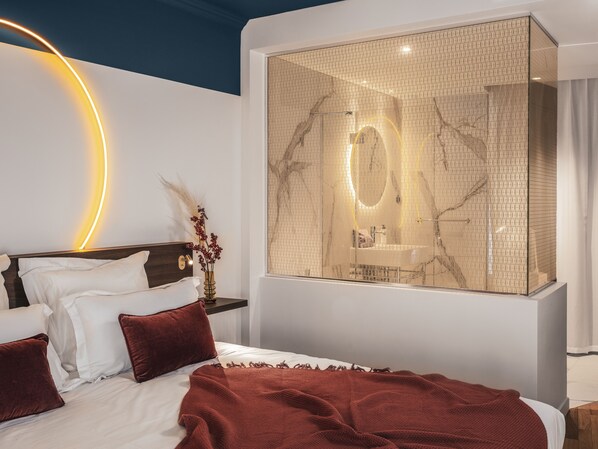 A modern bedroom with a large bed, a nightstand, and a wall-mounted mirror.