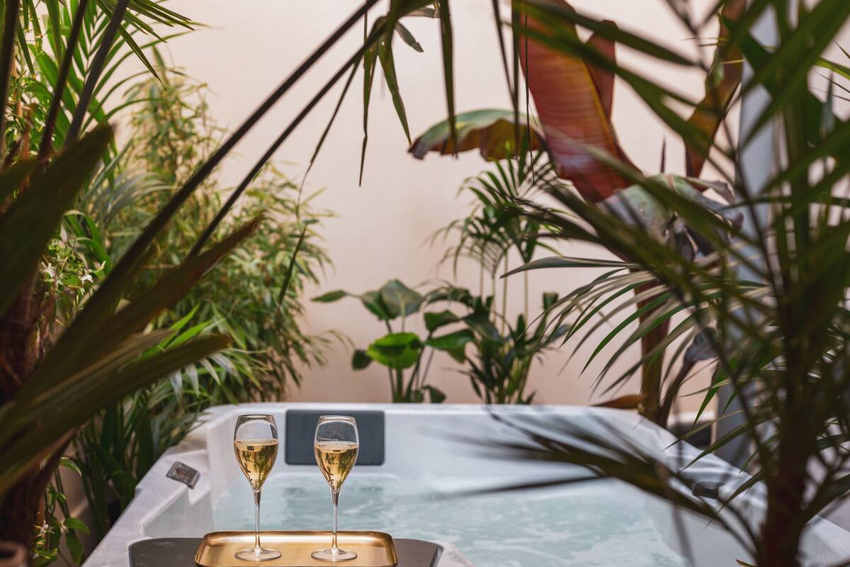 A hot tub with two glasses of champagne, surrounded by lush green plants.