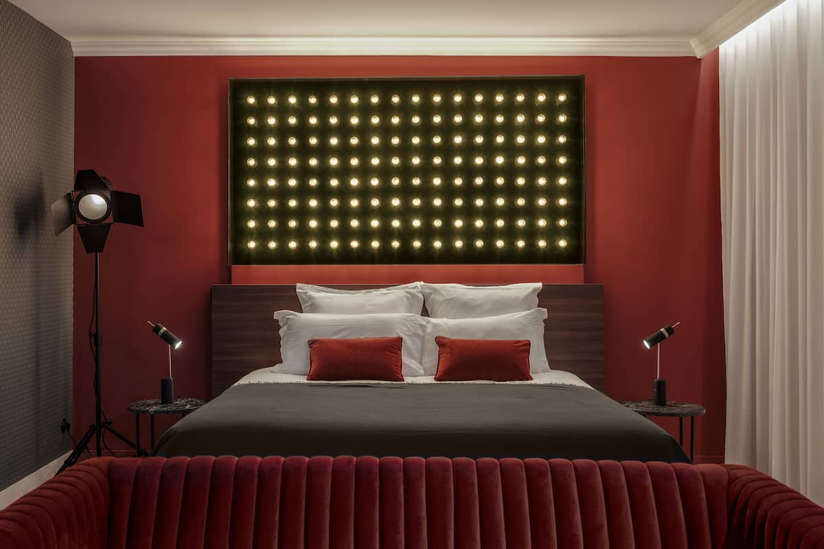 A modern hotel room with a large bed, red walls, and a unique illuminated headboard.