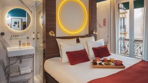 A hotel room with a bed, a bedside table with toiletries, a mirror, and a view of the outside. - Seven Hotel Paris (Paris)