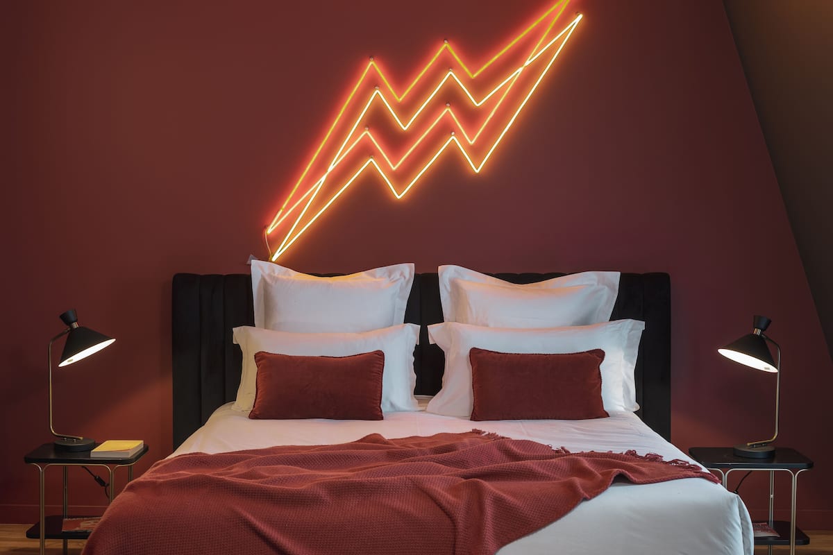 A modern bedroom with a bed, two bedside tables, and a neon light design on the wall.