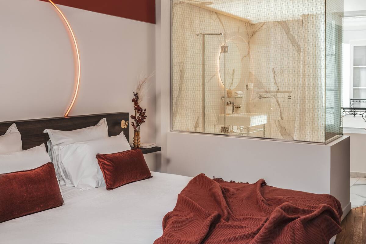 A modern hotel room with a large bed, a glass shower enclosure, and a curved neon light on the ceiling.