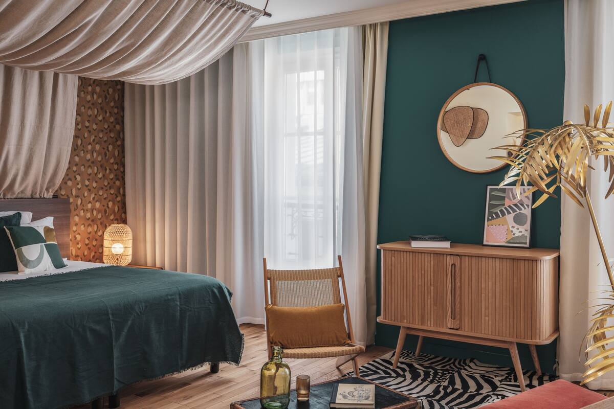 A bedroom with a bed, a chair, a wooden cabinet, and a large mirror on the wall.