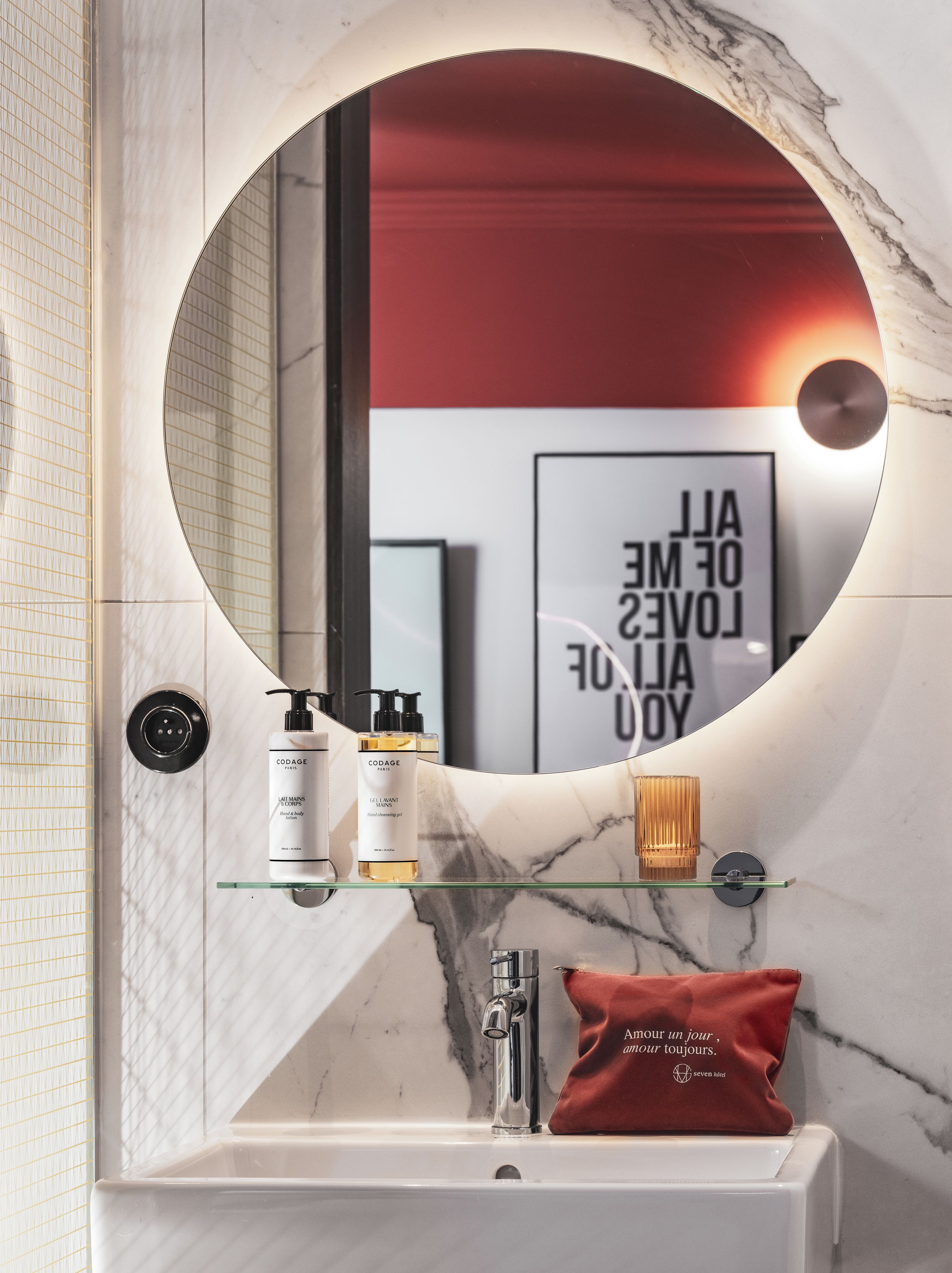 Une salle de bain avec un miroir rond, un lavabo et une étagère contenant des articles de toilette.