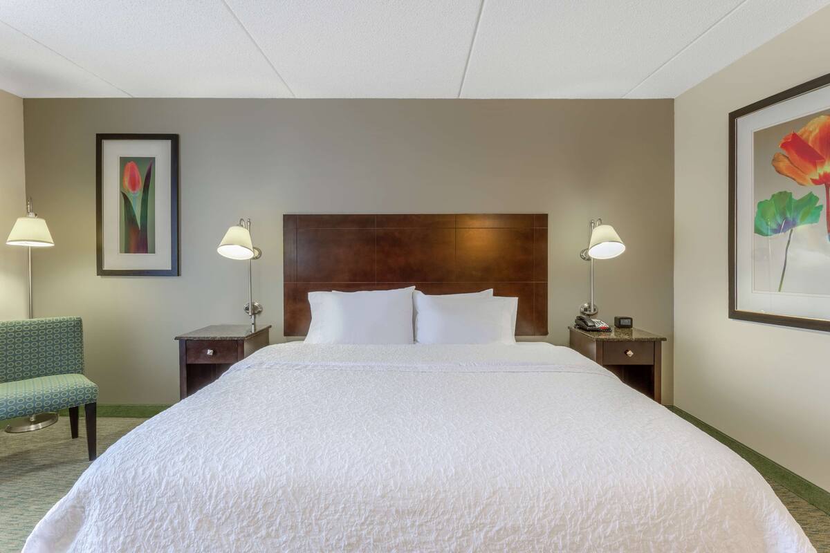 A hotel room with a large bed, two bedside tables, a chair, and wall-mounted lamps.