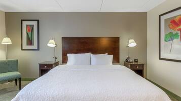 Una habitación de hotel con una cama grande, dos mesitas de noche, una silla y lámparas fijadas a la pared.