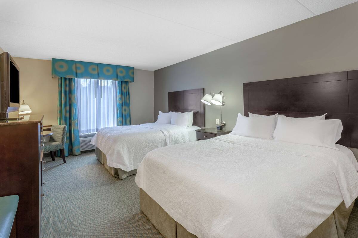 A hotel room with two beds, a desk, a chair, and a window with curtains.