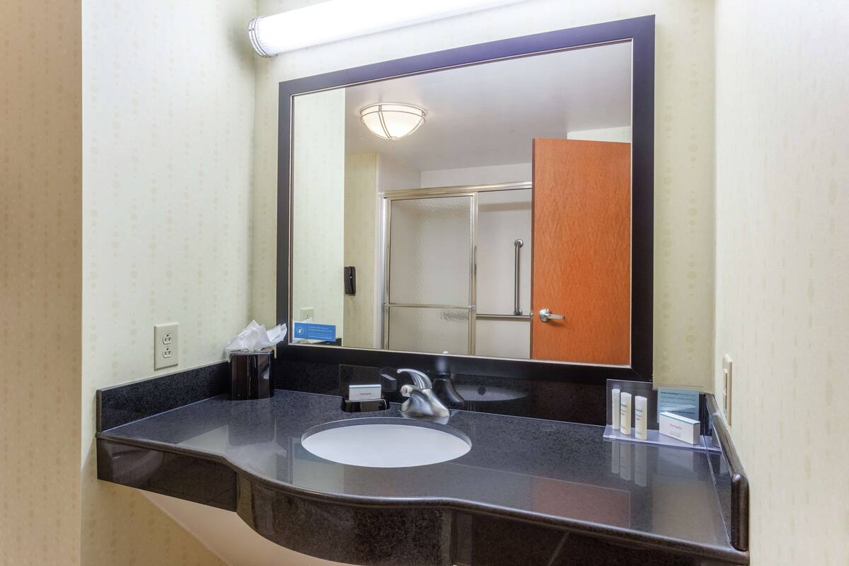 A hotel bathroom with a large mirror, a sink, and a shower visible in the reflection.