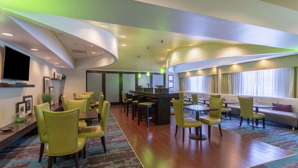 Eine moderne Hotelhalle mit Barbereich, Sitzgelegenheiten und einem Fernseher.