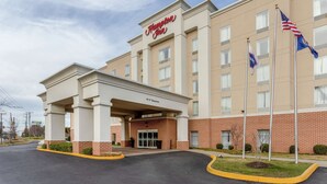 Ein Hampton Inn Hotel mit Backsteinfassade, einer überdachten Eingangsparte und mehreren Flaggen.