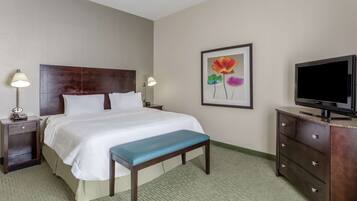 A hotel room with a bed, bedside lamps, a TV, a bench, and a painting on the wall.