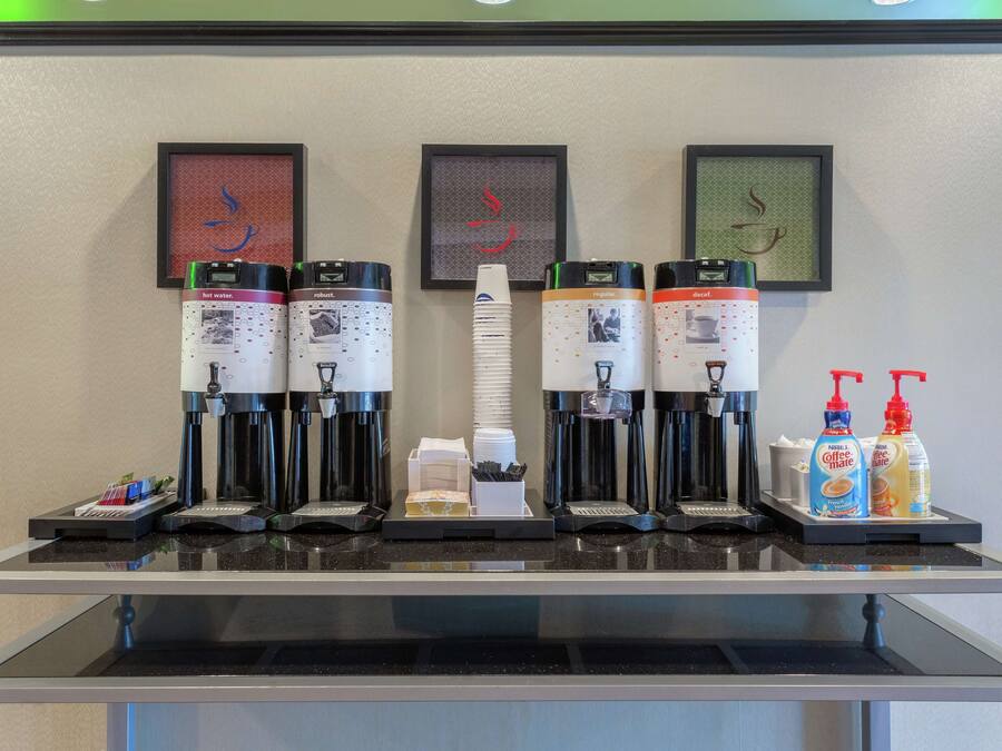 Una estación de café con varias máquinas de café, vasos desechables y condimentos.
