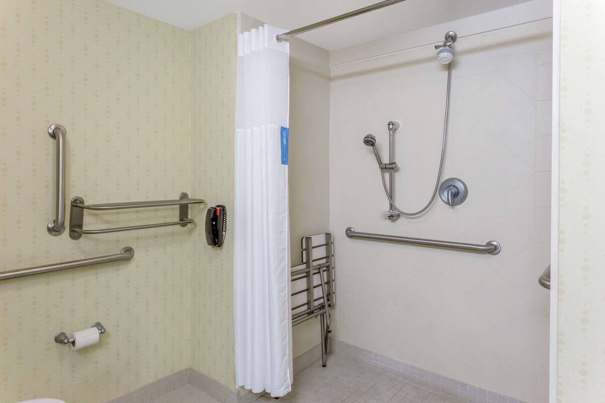 A bathroom with a shower, grab bars, a toilet, and a roll of toilet paper.