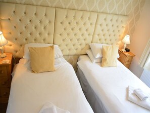A hotel room with two beds, each with a tufted headboard and white linens. There are bedside tables with lamps and a small clock on one of them. - Ashlea Guest House (Banbury)