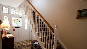 A staircase with white balusters and a wooden handrail, leading to a landing with a patterned rug and a small table. - Ashlea Guest House (Banbury)