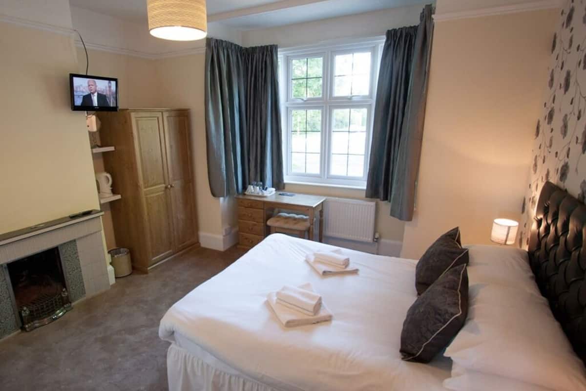 A hotel room with a bed, a television, a desk, a fireplace, and a window with curtains.