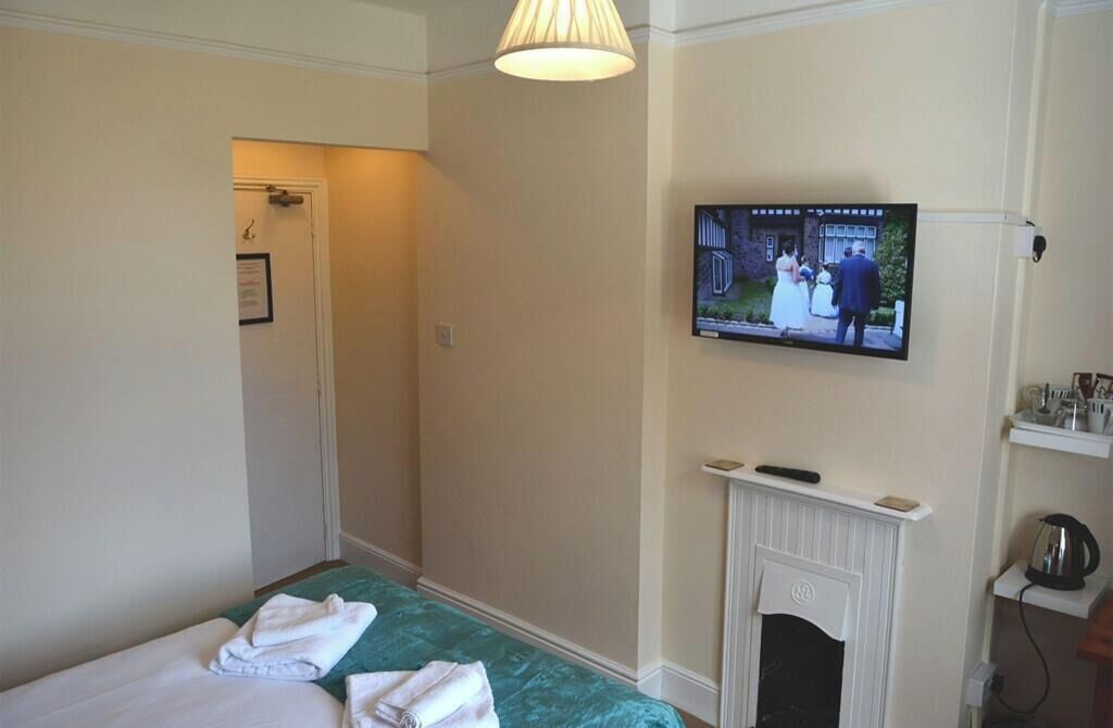 A hotel room with a bed, a television mounted on the wall, and a fireplace.