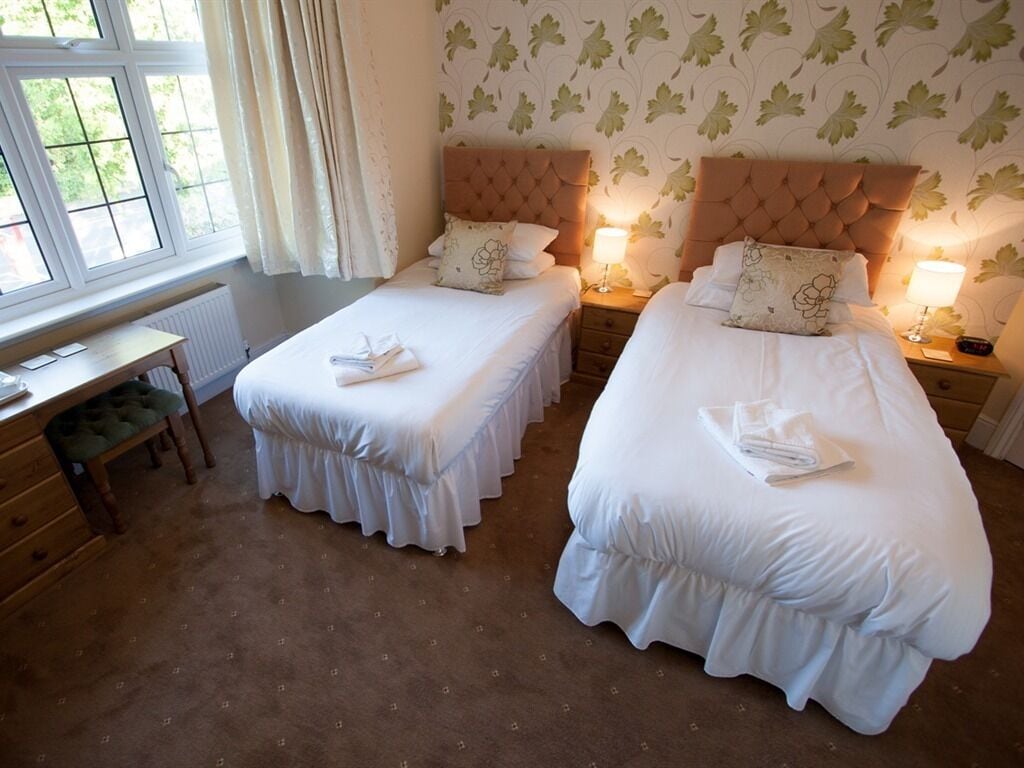 A hotel room with two single beds, a wooden desk, and a view of greenery through the window.