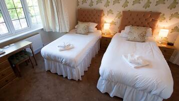 A hotel room with two single beds, a wooden desk, and a view of greenery through the window.