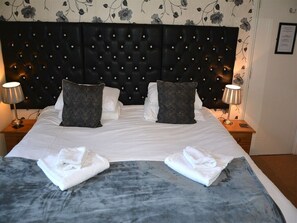 A hotel room with a tufted headboard, two pillows, a bed with white linens, and two bedside lamps. - Ashlea Guest House (Banbury)