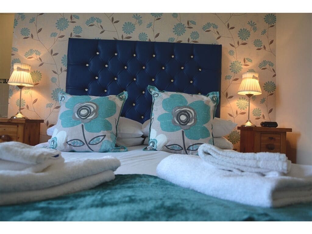 A neatly made bed with a tufted headboard, two floral pillows, and folded towels.