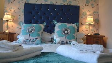 A neatly made bed with a tufted headboard, two floral pillows, and folded towels.