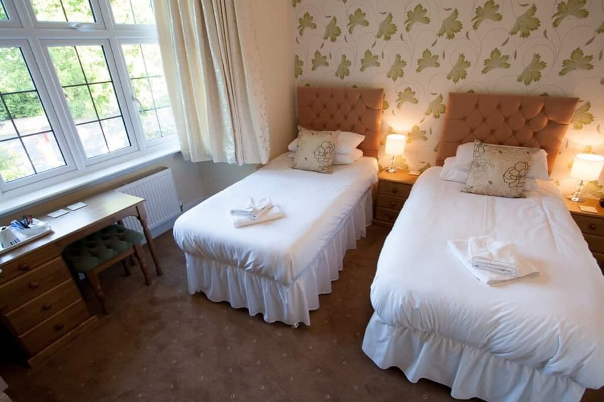 A hotel room with two single beds, a desk, and a view of greenery through the window.