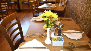 A dining table set with white napkins, silverware, and a vase of yellow flowers. - Ashlea Guest House (Banbury)