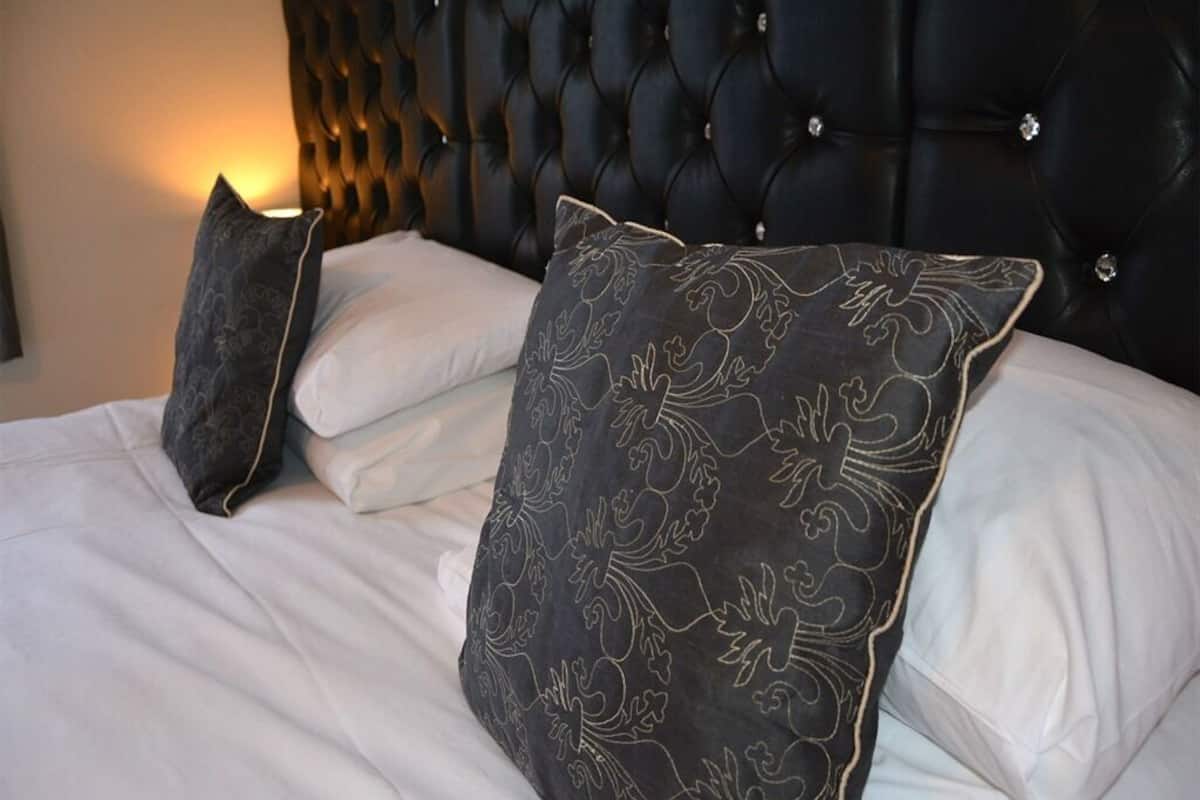 A bed with a tufted headboard, white linens, and patterned pillows.