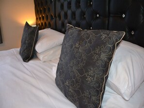 A bed with a tufted headboard, white linens, and patterned pillows. - Ashlea Guest House (Banbury)