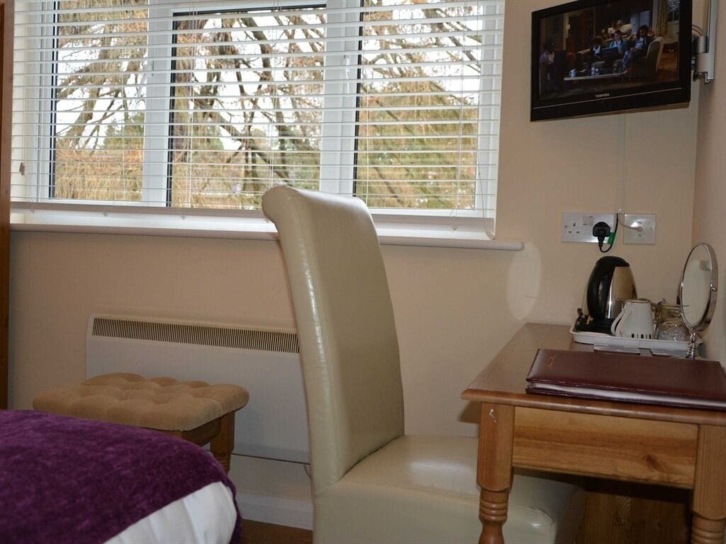Ein Zimmer mit Fenster, Heizkörper, Stuhl, Tisch und Fernseher.