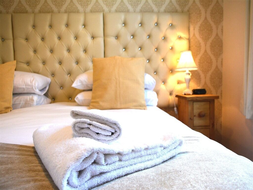 A neatly made bed with a tufted headboard, a folded towel, and a bedside table with a lamp.