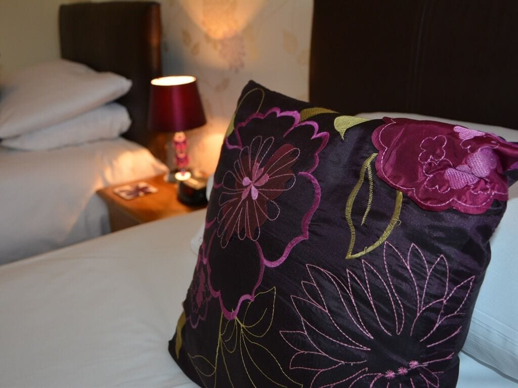 A bed with white linens and a decorative pillow with floral embroidery.