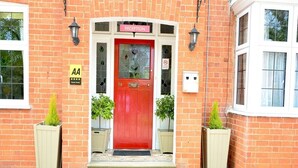 A red door with a reception sign, a 'AA' sign, and a 'Great House' sign on a brick building. - Ashlea Guest House (Banbury)